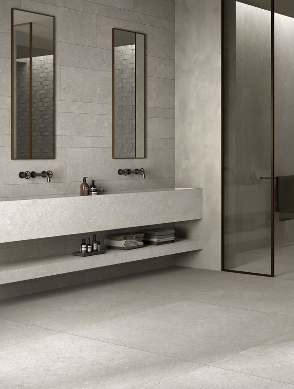 Long stone vanity with two basins, an open shelf, and large wall tiles
