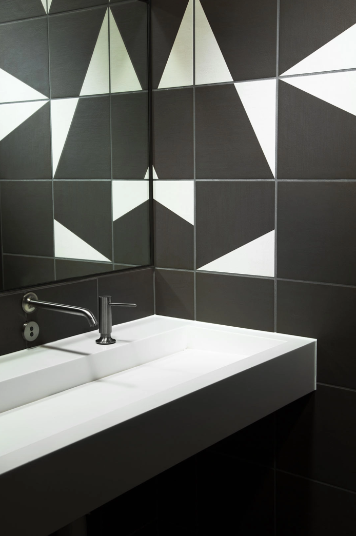 White trough basin against a wall of dark geometric tiles